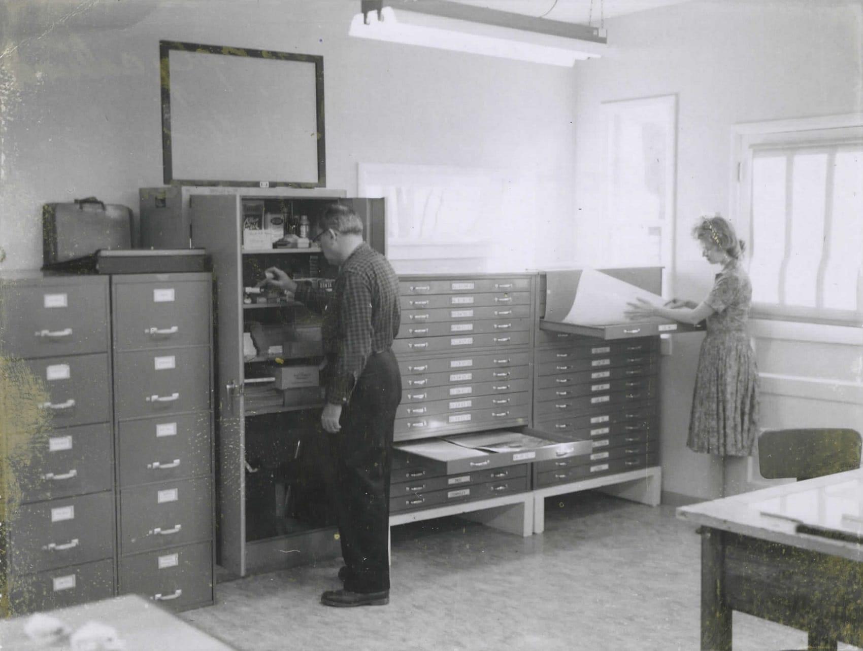 Patricia Bridges captioned this photo of her in the ACIC office at Lowell Observatory: “Jim Greenacre at the supply cabinet and yours truly (legless) at the filing cabinet across from my corner.” Photo courtesy of Patricia Bridges/Lowell Observatory.